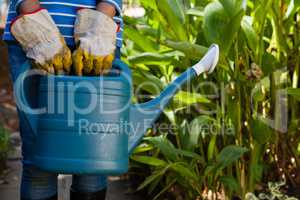 Midsection of senior woman standing with watering can against plants