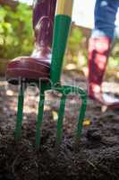 Low section of senior woman standing with garden fork on dirt