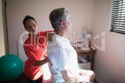 Young female therapist massaging back of senior male patient