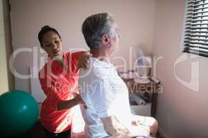 Young female therapist massaging back of senior male patient