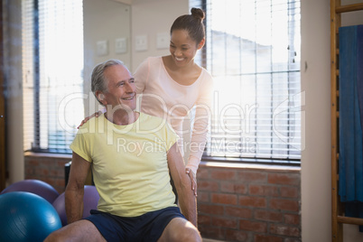 Smiling female therapist looking at senior male patient against window