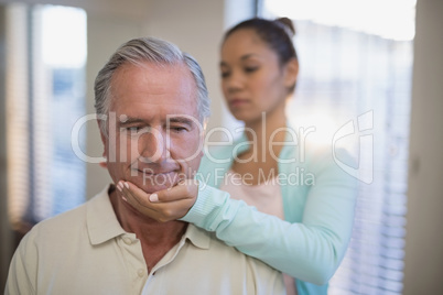 Young female therapist giving neck massage to senior patient