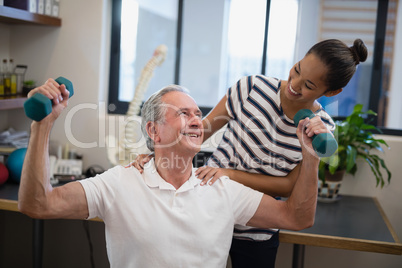 Smiling female doctor looking at senior male patient lifting dumbbells