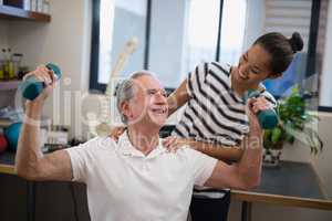 Smiling female doctor looking at senior male patient lifting dumbbells