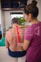 Female therapist applying elastic therapeutic tape on back of shirtless senior male patient