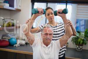 Female doctor looking at male patient lifting dumbbells