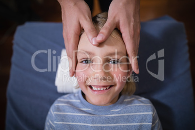 Overhead view of smiling boy receiving head massage from female therapist