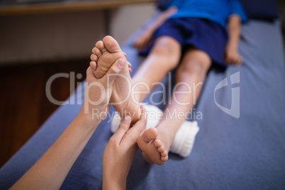 High angle view of boy lying on bed receiving foot massage from female therapist