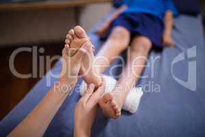 High angle view of boy lying on bed receiving foot massage from female therapist