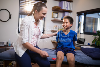 Smiling female therapist looking at boy while hitting at knee with reflex hammer