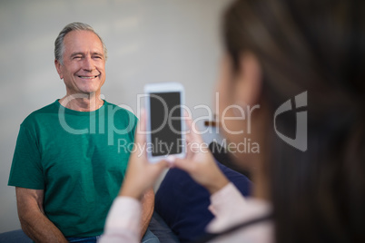 Female therapist photographing senior male patient from mobile phone