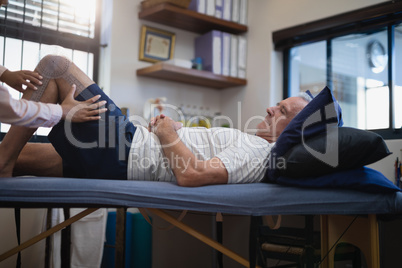 Hands of female therapist measuring knee while senior male patient lying on bed