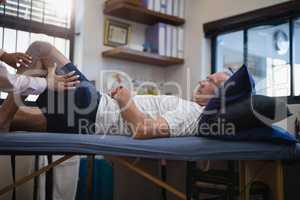 Hands of female therapist measuring knee while senior male patient lying on bed