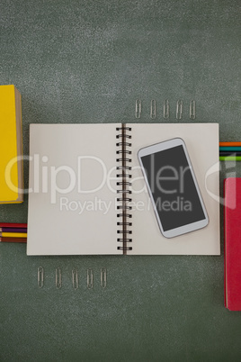 Various school supplies and mobile phone arranged on chalkboard Various school supplies and mobile phone arranged on chalkboard