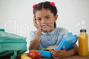 Schoolgirl sitting with tiffin box against white background