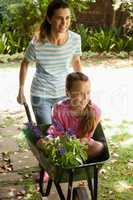 Smiling mother pushing girl with flowers sitting in wheelbarrow