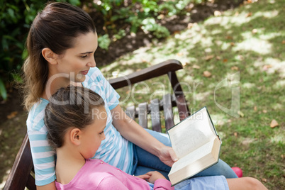 Tilt shot of mother reading novel to daughter on wooden bench