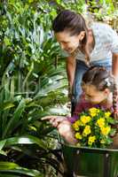 Mother looking while daughter sitting in wheelbarrow pointing towards plants
