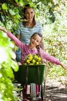 Girl enjoying with arms outstretched while smiling mother pushing wheelbarrow