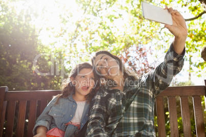 Low angle view of woman taking selfie with daughter while making faces against trees