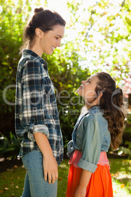 Side view of smiling mother and daughter standing in backyard
