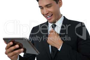 Happy businessman holding necktie while using tablet computer