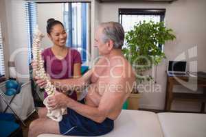 Smiling female therapist looking at shirtless male patient holding artificial spine