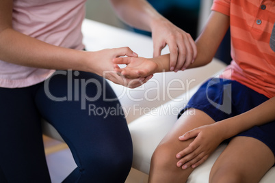 Midsection of female therapist examining wrist with boy sitting on bed