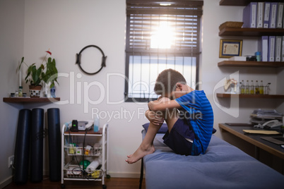 Side view of boy sitting on bed in pain