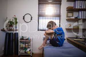 Side view of boy sitting on bed in pain