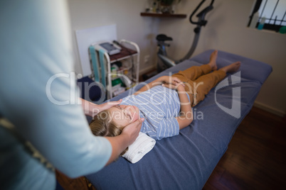 High angle view of female physiotherapist giving head massage to boy lying on bed