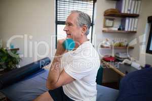Side view of senior patient lifting dumbbell while sitting on bed