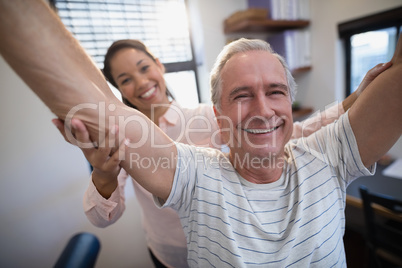 Portrait of smiling senior male patient and female doctor with arms raised