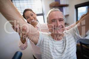 Portrait of smiling senior male patient and female doctor with arms raised