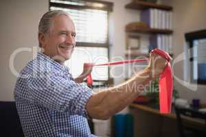 Smiling senior male patient pulling red resistance band