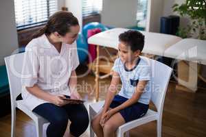Female therapist and boy talking while sitting on chairs