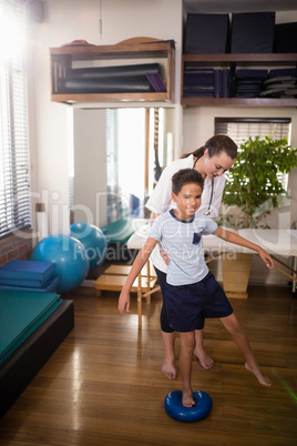 Female therapist holding boy standing on blue stress ball