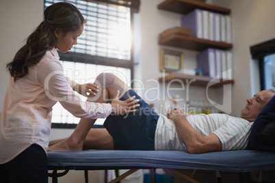 Female therapist measuring knee while senior male patient lying on bed