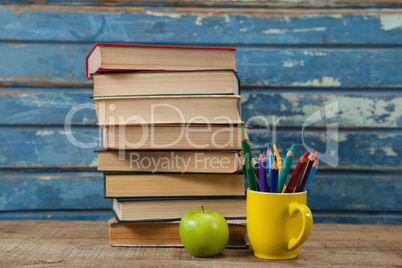 Book stack, color pencils and apple on wooden table