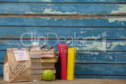 Stack of books, apple, water bottle, spectacles and lunch bag