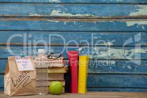 Stack of books, apple, water bottle, spectacles and lunch bag