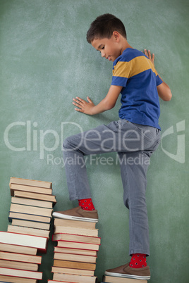 Schoolboy climbing steps of books stack