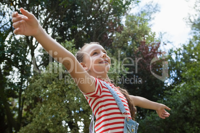 Low angle view of smiling girl with arms outstretched standing against trees