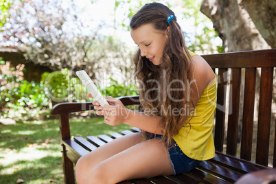 Smiling girl using smartphone while sitting on wooden bench