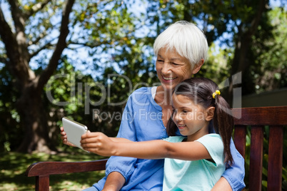 Smiling girl taking selfie with grandmother while sitting on bench