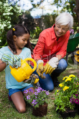 Smiling senior woman looking at girl watering flowers