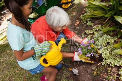 High angle view of girl standing with watering can by grandmother planting