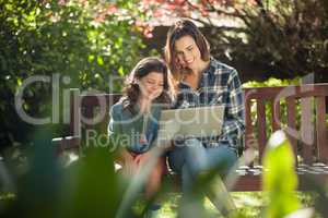 Smiling mother and daughter using laptop while sitting on wooden bench