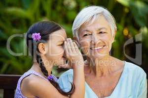 Granddaughter whispering in ears of smiling grandmother