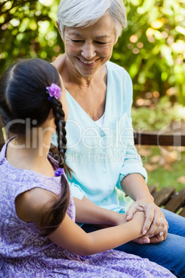 Smiling grandmother holding hands of granddaughter while sitting on bench